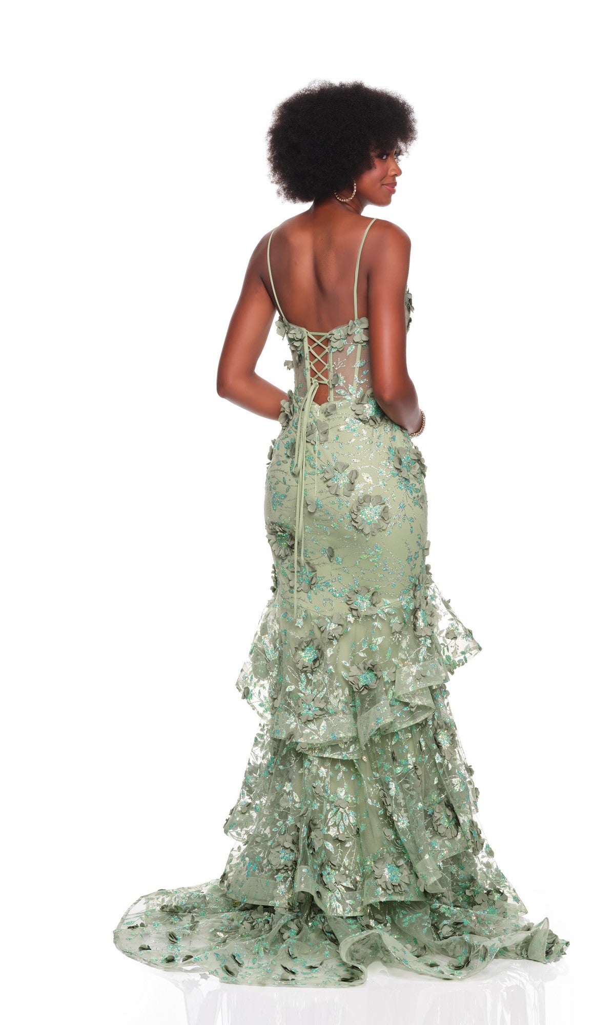 A woman faces away from the camera in a Dave and Johnny 12379 long prom dress, light green with 3D floral applique, lace-up back, and ruffled train, set against a white background.